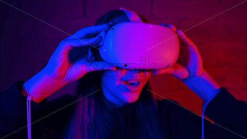 A young woman is excited while putting on VR glasses, controllers. Red and blue illumination. Slow motion virtual reality - Starpik Stock