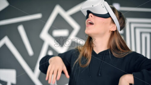 A young woman is excited while putting on VR glasses, controllers. Slow motion virtual reality - Starpik Stock