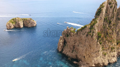 Aerial drone cinematic view of the Tyrrhenian sea coast of Capri, Italy. Rocky cliffs, blue water, floating boats, greenery - Starpik Stock