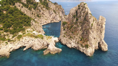 Aerial drone cinematic view of the Tyrrhenian sea coast of Capri, Italy. Rocky cliffs, blue water, floating boats, greenery - Starpik Stock