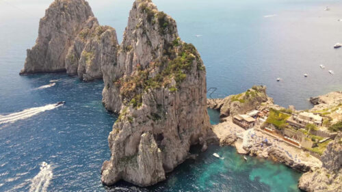 Aerial drone cinematic view of the Tyrrhenian sea coast of Capri, Italy. Rocky cliffs, blue water, floating boats, greenery - Starpik Stock
