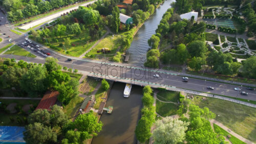 Aerial drone view of Bega river in Timisoara, Romania. View of the river with floating boat, greenery on the both sides of the river and bridge with moving cars, cityscape - Starpik Stock