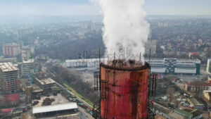 Aerial drone view of Chisinau. Tube of the thermal station with smoke coming out. Industrial zone near it and cityscape on the background. Cloudy weather. Moldova - Starpik Stock