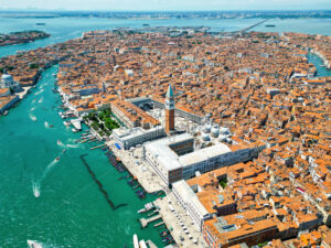 Aerial drone view of Venice, Italy. Water channels with multiple floating and moored boats, historical city centre with St Mark’s Square and other old buildings and narrow streets - Starpik Stock