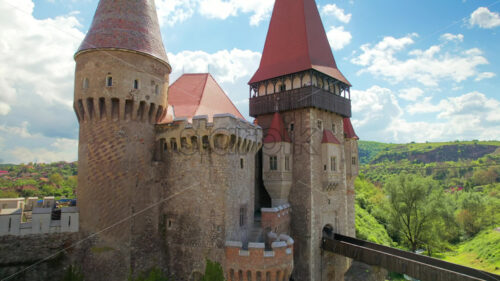 Aerial drone view of the Corvin Castle located in Hunedoara, Romania. Bridge leading to the entrance. Greenery and buildings around - Starpik Stock