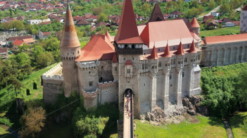 Aerial drone view of the Corvin Castle located in Hunedoara, Romania. People walking on the bridge leading to the entrance. Greenery and buildings around - Starpik Stock