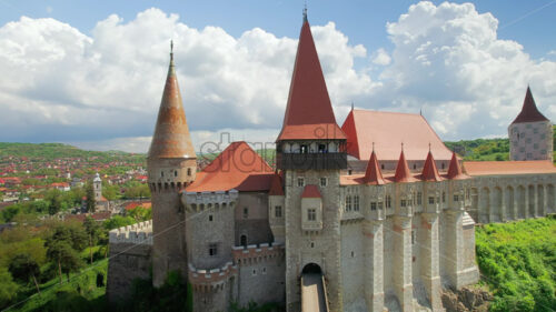 Aerial drone view of the Corvin Castle located in Hunedoara, Romania. People walking on the bridge leading to the entrance. Greenery and buildings around - Starpik Stock