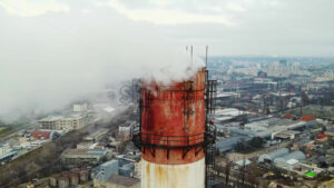 Aerial drone view of thermal station with smoke coming out of the tube. Buildings, roads and bare trees on the background. Cloudy weather. Chisinau, Moldova - Starpik Stock