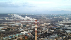 Aerial drone view of thermal station with smoke coming out of the tube. Buildings, roads, lake and bare trees on the background. Cloudy weather. Chisinau, Moldova - Starpik Stock