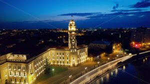 Areal drone view of the Town Hall in Oradea downtown at night, Romania. People on top on the City Hall Tower , illumination and Crisul Repede river - Starpik Stock