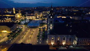 Areal drone view of the Unirii Square in Oradea downtown at night, Romania. Moon Church, Cathedral of St. Nicholas and other historical buildings, illumination - Starpik Stock