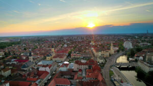 Areal drone view of the Unirii Square in Oradea downtown at sunset, Romania. King Ferdinand I statue, Saint Ladislaus Church, Town Hall and other historical buildings, walking people - Starpik Stock