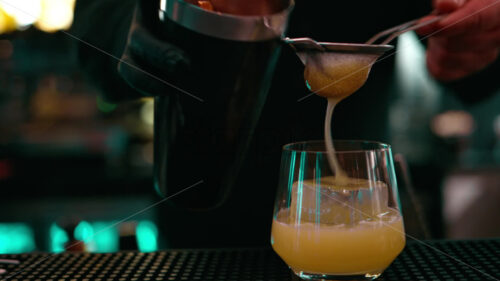 Bartender pouring whiskey cocktail into a glass with big cube of ice from a shaker mixer - Starpik Stock