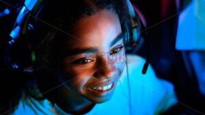 Black teen smiling girl in headset playing video games in video game club - Starpik