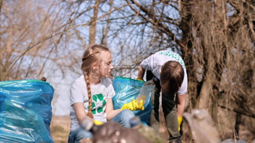 Boy and girl collecting plastic garbage in a bag in a polluted clearing, recycling signs on the T-shirts. Slow motion - Starpik
