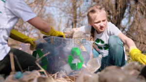 Boy and girl collecting plastic garbage in a container in a polluted clearing, recycling signs on the T-shirts. Slow motion - Starpik