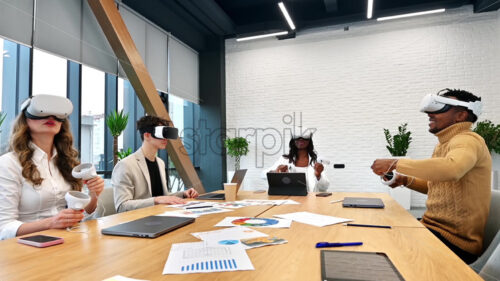 Business conference in VR in an office. Multiracial group of people using VR glasses and controllers, papers and gadgets on the table. Slow motion, virtual reality - Starpik Stock