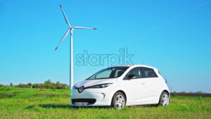 CHISINAU, MOLDOVA – APRIL 26, 2021: Renault Zoe electric car and electric wind mill eolian working, green field - Starpik Stock