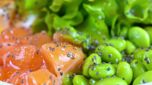Close up poke bowl with salmon fish, avocado, feta cheese, mango, tomatoes, salad, and green edamame beans - Starpik Stock