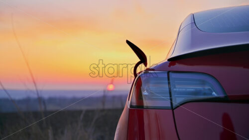 Close view of a man plugging charging cable into a parked red electric car at sunset - Starpik