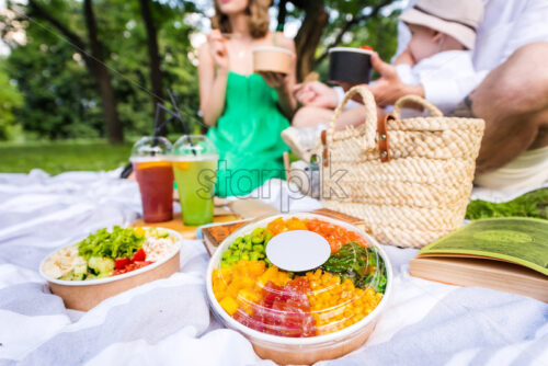 Close view of poke bowls on a blanket, family in the background - Starpik Stock