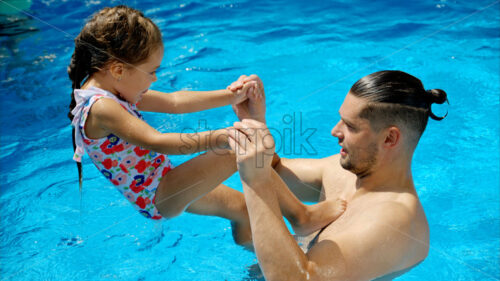 Father and daughter resting and swimming in a pool in summer - Starpik Stock