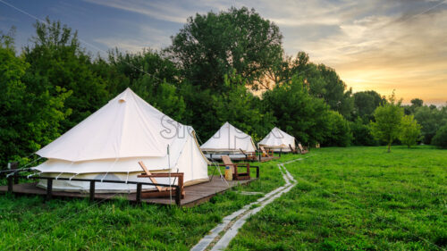 Glamping tents in nature with green grass at sunset. Summer season - Starpik Stock