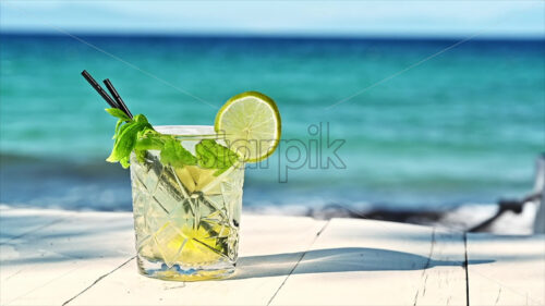 Green mojito cocktail with lemon slice on a table by the blue green sea video - Starpik Stock