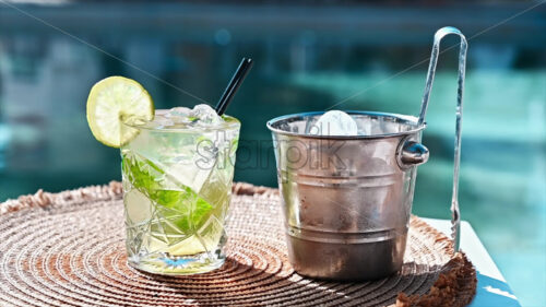 Green mojito cocktail with lemon slice on a table with ice bucket by the pool video - Starpik Stock