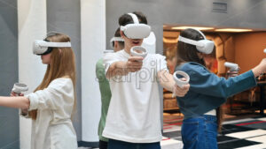 Group of four teens with VR headset and controllers playing games in a team on a VR arena. Slow motion - Starpik Stock