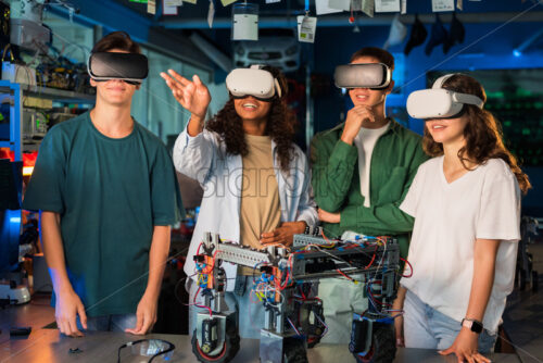 Group of young people in VR glasses doing experiments in robotics in a laboratory. Robot on the table - Starpik Stock