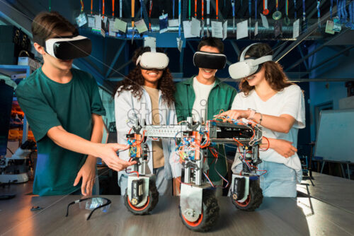 Group of young people in VR glasses doing experiments in robotics in a laboratory. Robot on the table - Starpik Stock