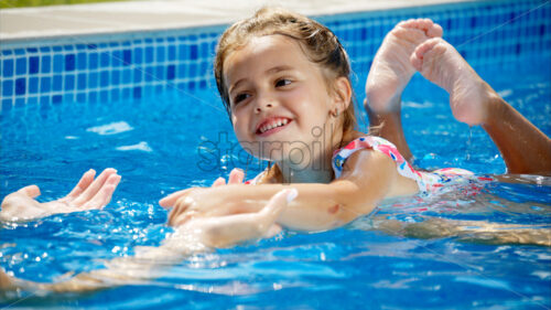 Little girl in sunglasses learning to swim in a pool with her mother - Starpik Stock
