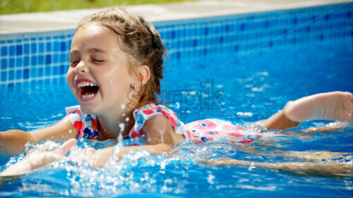 Little girl in sunglasses learning to swim in a pool with her mother - Starpik Stock