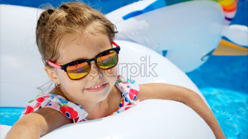 Little girl in sunglasses resting on white pool balloon - Starpik Stock