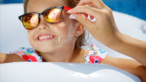 Little girl in sunglasses resting on white pool balloon - Starpik Stock