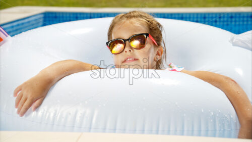 Little girl in sunglasses resting on white pool balloon - Starpik Stock