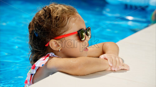 Little girl in sunglasses resting on white pool balloon - Starpik Stock