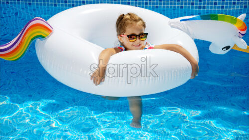 Little girl in sunglasses resting on white pool balloon - Starpik Stock