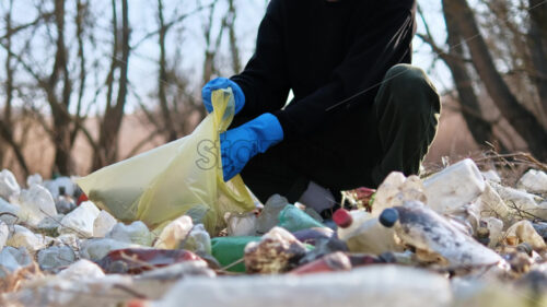 Man collecting scattered plastic bottles from the ground in the nature - Starpik