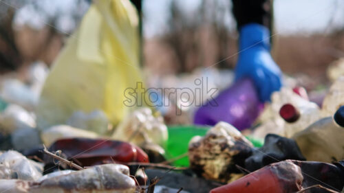 Man collecting scattered plastic bottles from the ground in the nature - Starpik