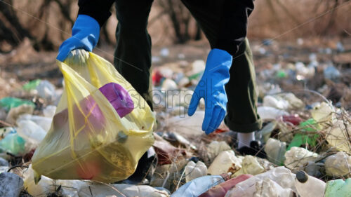 Man collecting scattered plastic bottles from the ground in the nature - Starpik