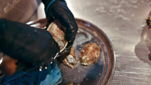 Man hands cleaning and opening oysters with special knife at seafood restaurant, slow motion - Starpik Stock