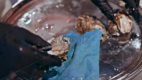 Man hands cleaning and opening oysters with special knife at seafood restaurant, slow motion - Starpik Stock