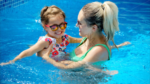 Mother and daughter resting and swimming in a pool in summer - Starpik Stock