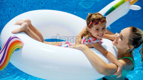 Mother and daughter resting and swimming in a pool in summer - Starpik Stock