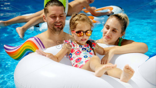 Mother with father and daughter resting and swimming in a pool in summer - Starpik Stock