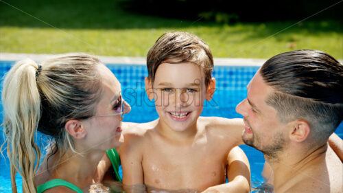 Mother with father and son resting and swimming in a pool in summer, happy family kissing - Starpik Stock