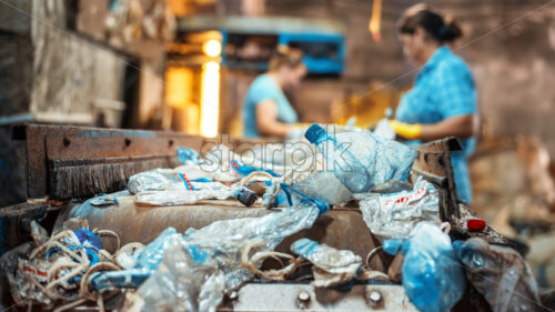 Plastic garbage on a conveyor belt at waste recycling factory. Workers on the background - Starpik Stock