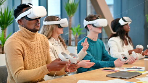 Premium stock video footage – Business conference in VR in an office. Multiracial group of people using VR glasses and controllers, papers and gadgets on the table. Slow motion, virtual reality - Starpik Stock